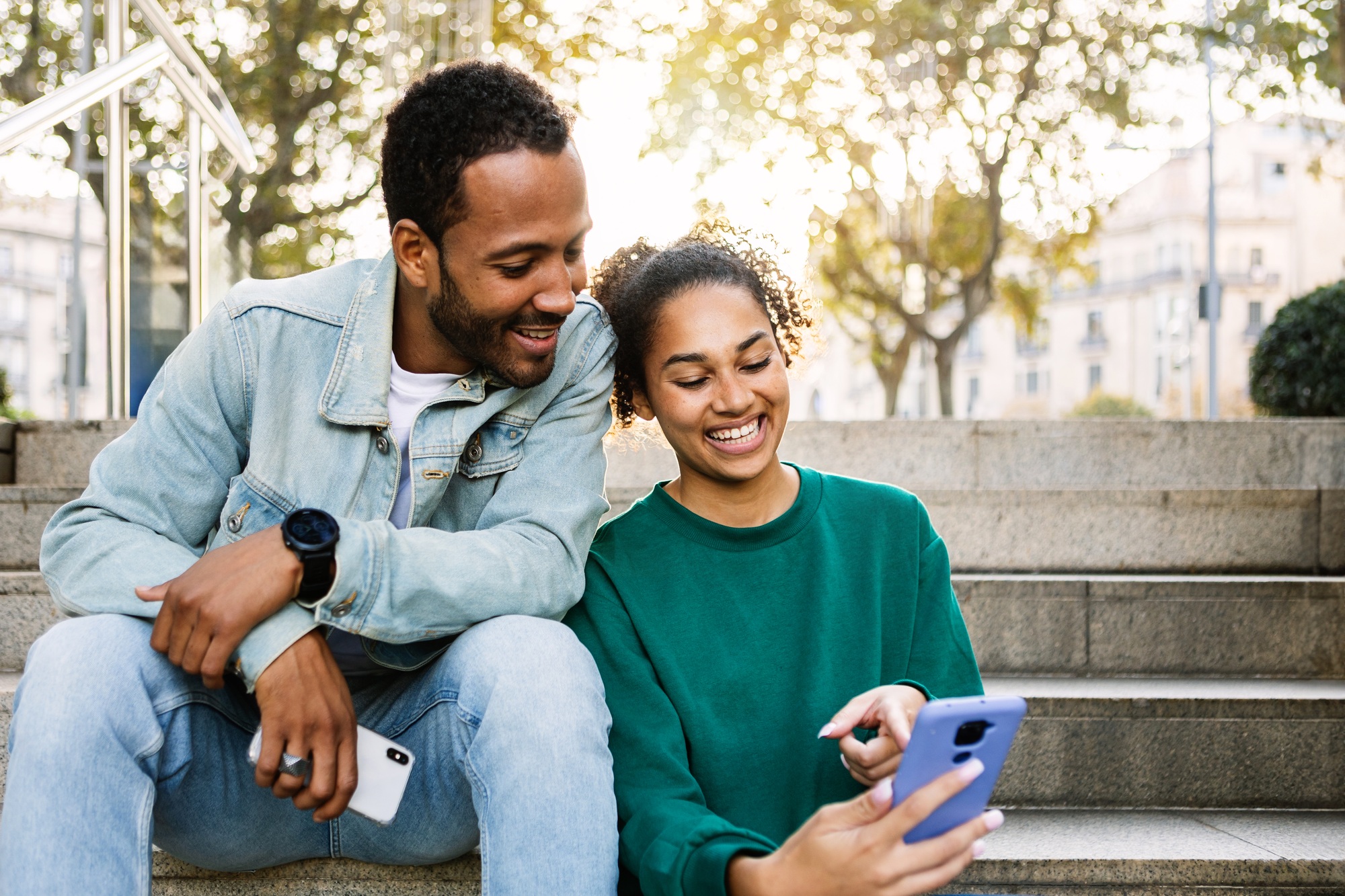 Two young latin american people using smart phone together sitting outdoors